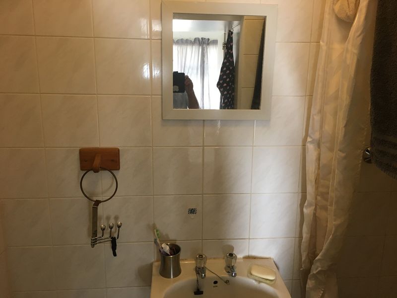 A dated bathroom featuring tiled walls, a pedestal basin with dual-handle taps, and a wall-mounted mirror.