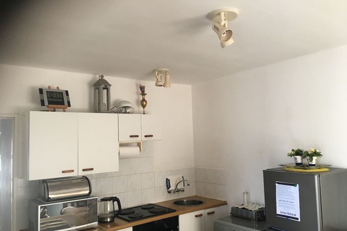 A compact kitchen featuring white cabinetry, a built-in oven with electric hob, stainless steel sink, and tiled splashback.
