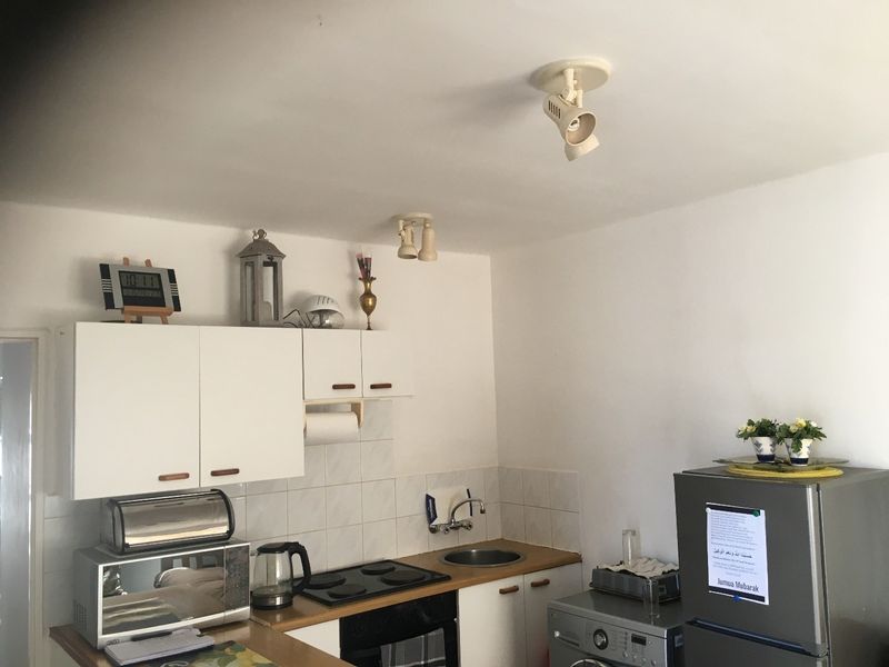 A compact kitchen featuring white cabinetry, a built-in oven with electric hob, stainless steel sink, and tiled splashback.