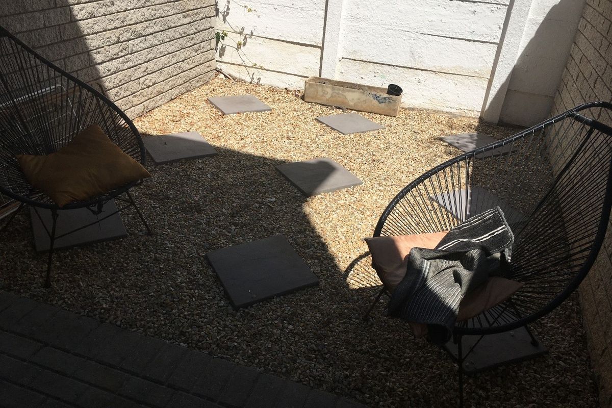 A small, low-maintenance rear courtyard area featuring gravel ground cover, concrete stepping stones, and enclosed by brick boundary walls.