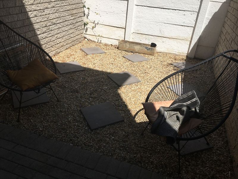 A small, low-maintenance rear courtyard area featuring gravel ground cover, concrete stepping stones, and enclosed by brick boundary walls.