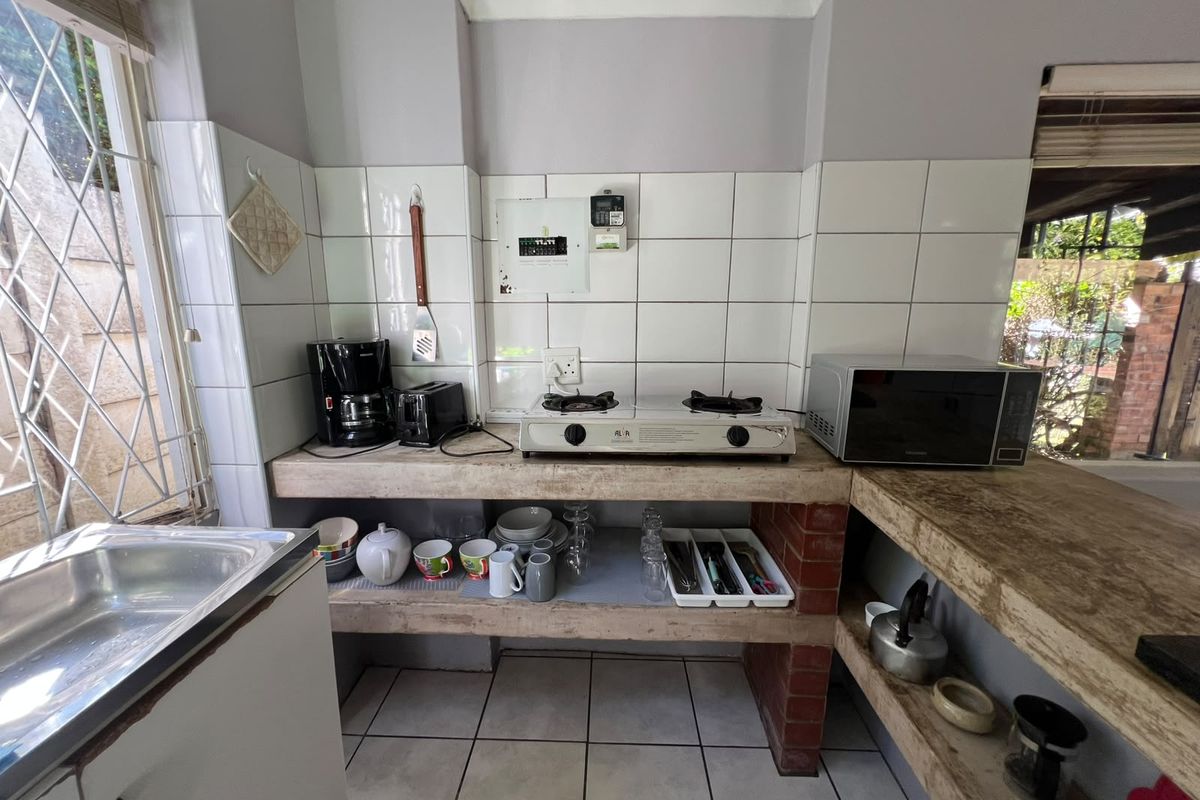 Compact kitchen area featuring concrete and brick shelving, tiled splashback, stainless steel sink, and gas cooktop, offering a functional but dated utility space.