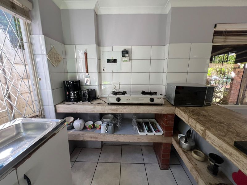 Compact kitchen area featuring concrete and brick shelving, tiled splashback, stainless steel sink, and gas cooktop, offering a functional but dated utility space.