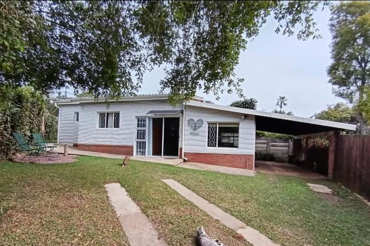 Rear view of the cottage featuring a brick base, attached carport, and sliding door access to the garden area.