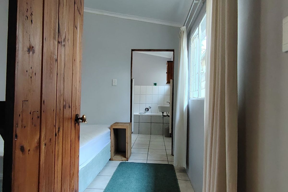 A bedroom featuring tiled flooring and direct access to an en-suite bathroom, with a timber door and window providing natural light.