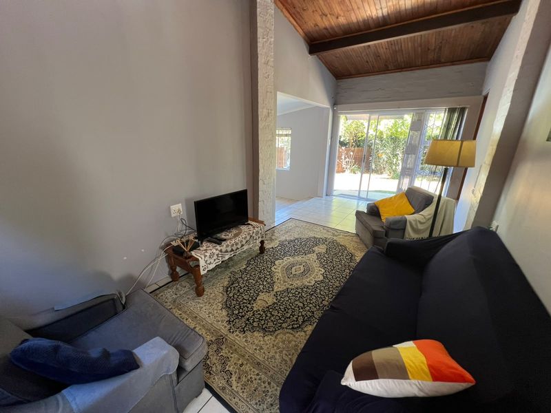 Living room featuring a high exposed timber rafter ceiling, stone-clad feature pillar, and sliding glass doors providing access to the rear garden.