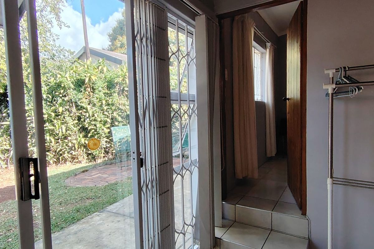 Interior view of a living area featuring tiled flooring, a sliding glass door with security gate, and access to an adjacent room via steps.