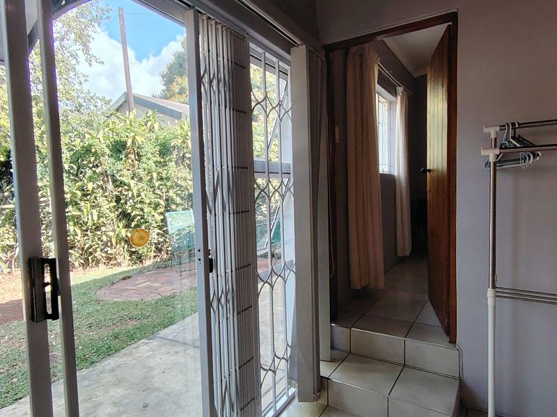 Interior view of a living area featuring tiled flooring, a sliding glass door with security gate, and access to an adjacent room via steps.