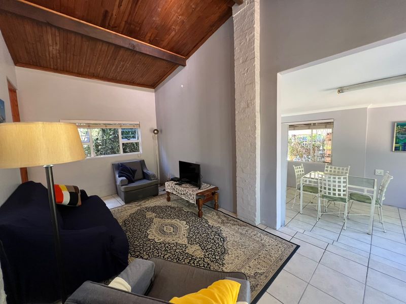 Open plan living and dining area featuring a high raked timber ceiling, painted brick column, and neutral tiled flooring throughout.