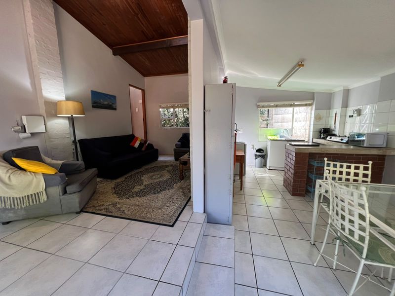 Open-plan living and kitchen area featuring exposed timber ceilings, tiled flooring, and a brick breakfast bar in a functional cottage layout.