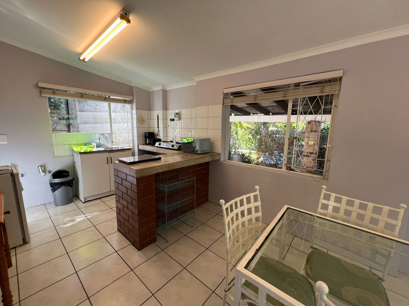A functional kitchen featuring a brick breakfast bar, tiled backsplash, and tiled flooring, with natural light provided by windows with security bars.