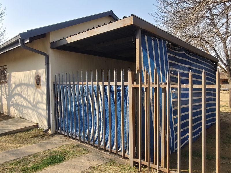Rear view of the property featuring a covered patio area enclosed with temporary screening and perimeter security fencing.