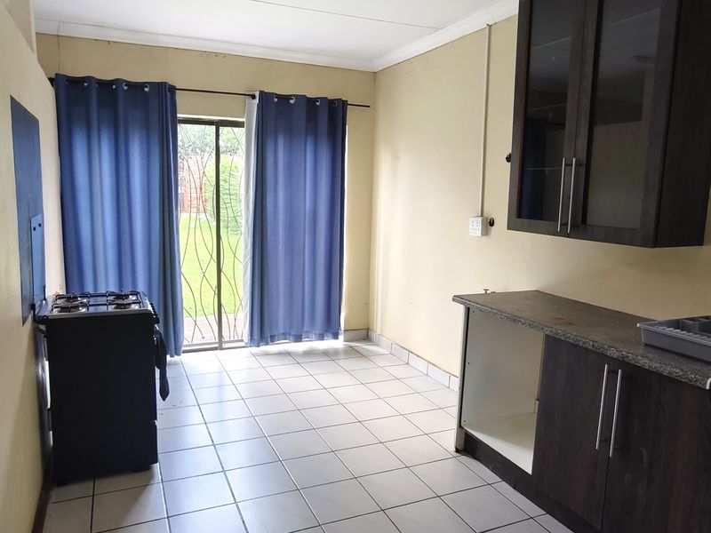 A functional kitchen area featuring dark cabinetry, tiled flooring, and direct access to the garden through a sliding glass door.