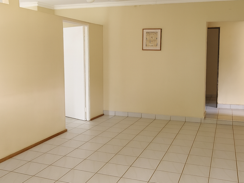 An empty, neutrally painted living area featuring ceramic floor tiles, coved ceilings, and multiple doorways leading to adjacent rooms.