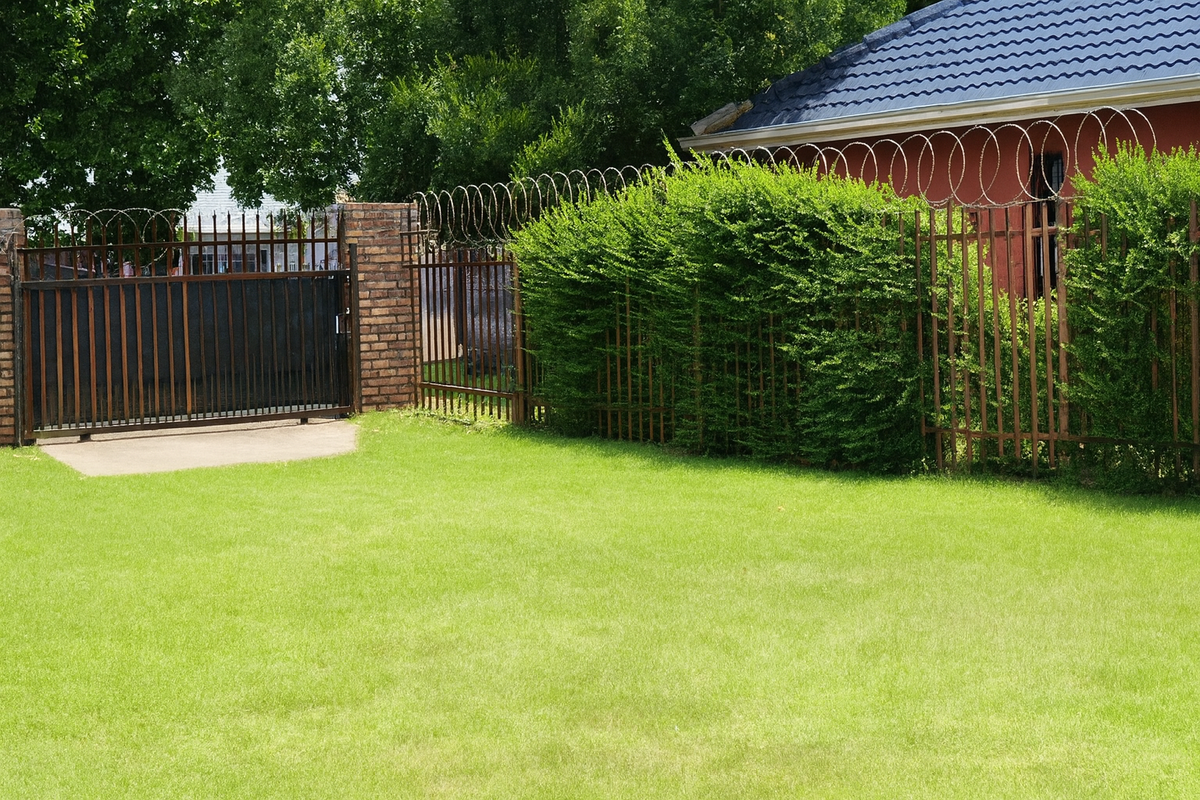 A rear garden area featuring a well-maintained lawn, enclosed by brick walls and metal security fencing with razor wire.