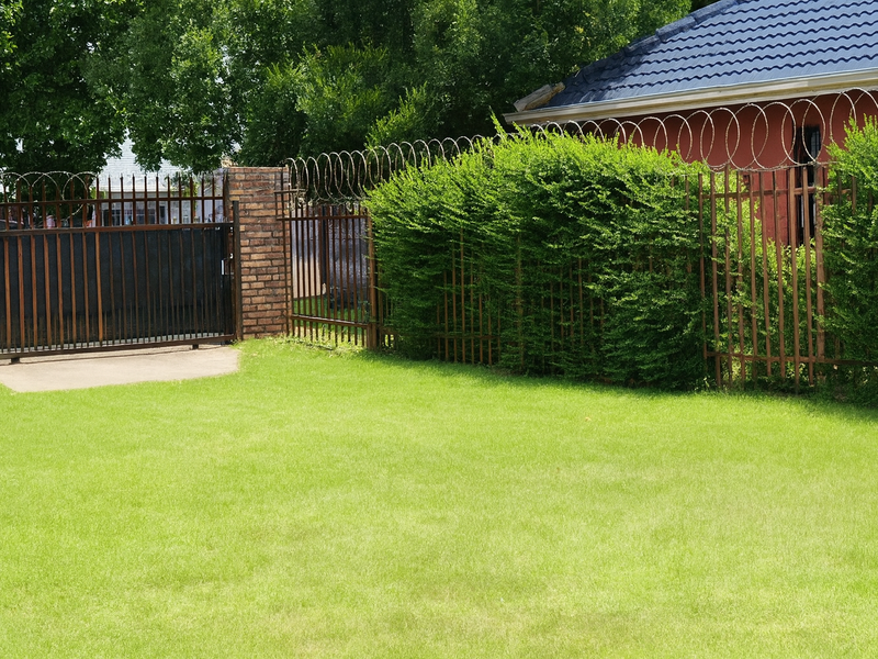 A rear garden area featuring a well-maintained lawn, enclosed by brick walls and metal security fencing with razor wire.