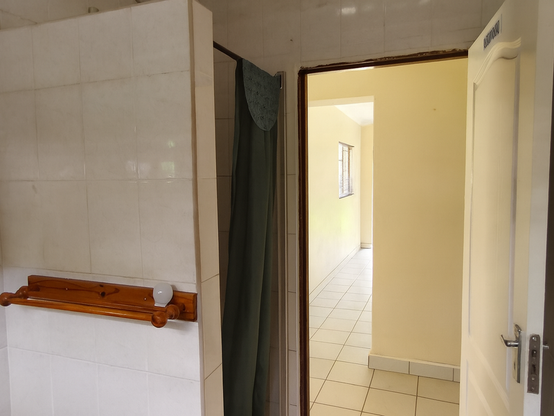 A functional bathroom space featuring tiled walls and flooring, with a shower partition and direct access to the adjacent hallway.