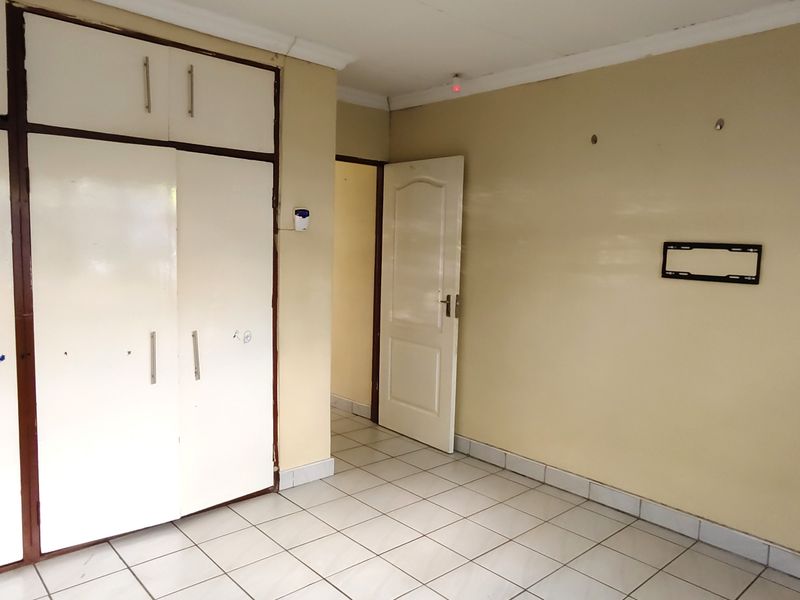 An empty bedroom featuring built-in cupboards, tiled flooring, and neutral wall finishes, ready for personalization or staging.