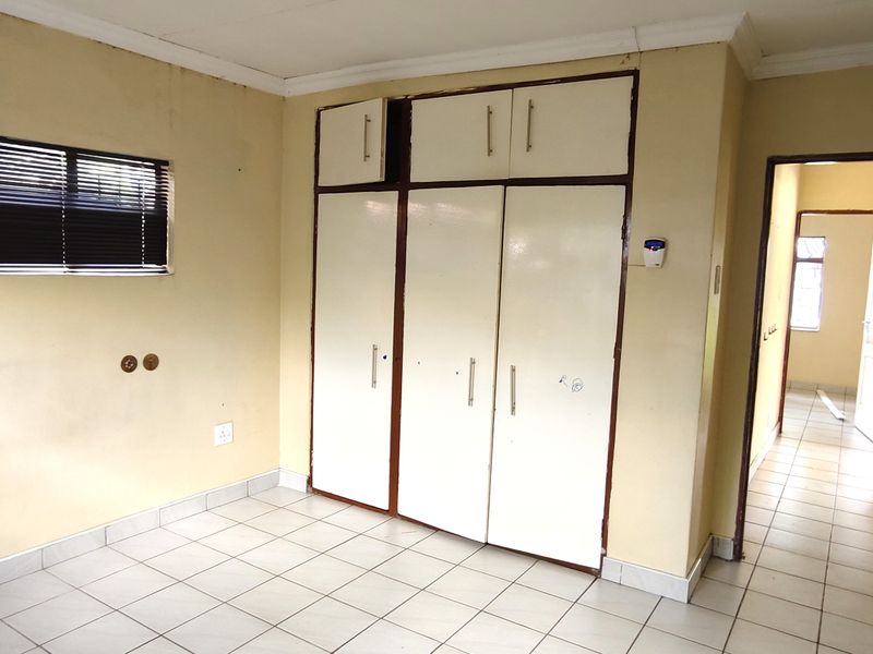 An empty bedroom featuring tiled flooring, built-in cupboards, and venetian blinds, requiring cosmetic updates to the wall finishes.
