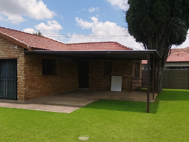 Rear view of the property featuring a facebrick exterior, terracotta tiled roof, and a covered patio area overlooking a well-maintained lawn.