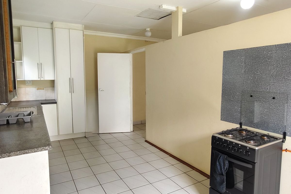 A functional kitchen area featuring tiled flooring, built-in cabinetry, and a freestanding gas stove with a wall-mounted splashback.