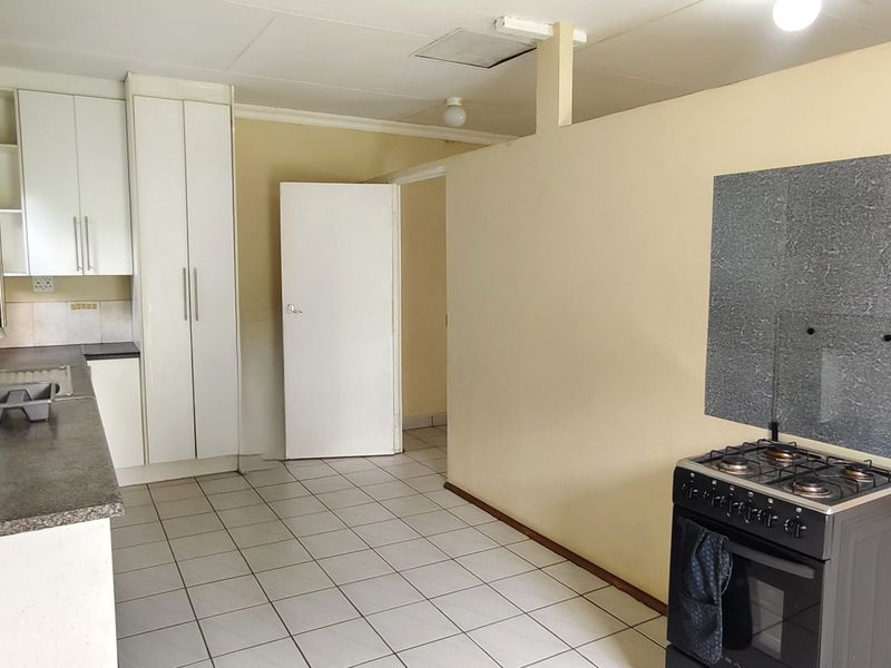 A functional kitchen area featuring tiled flooring, built-in cabinetry, and a freestanding gas stove with a wall-mounted splashback.
