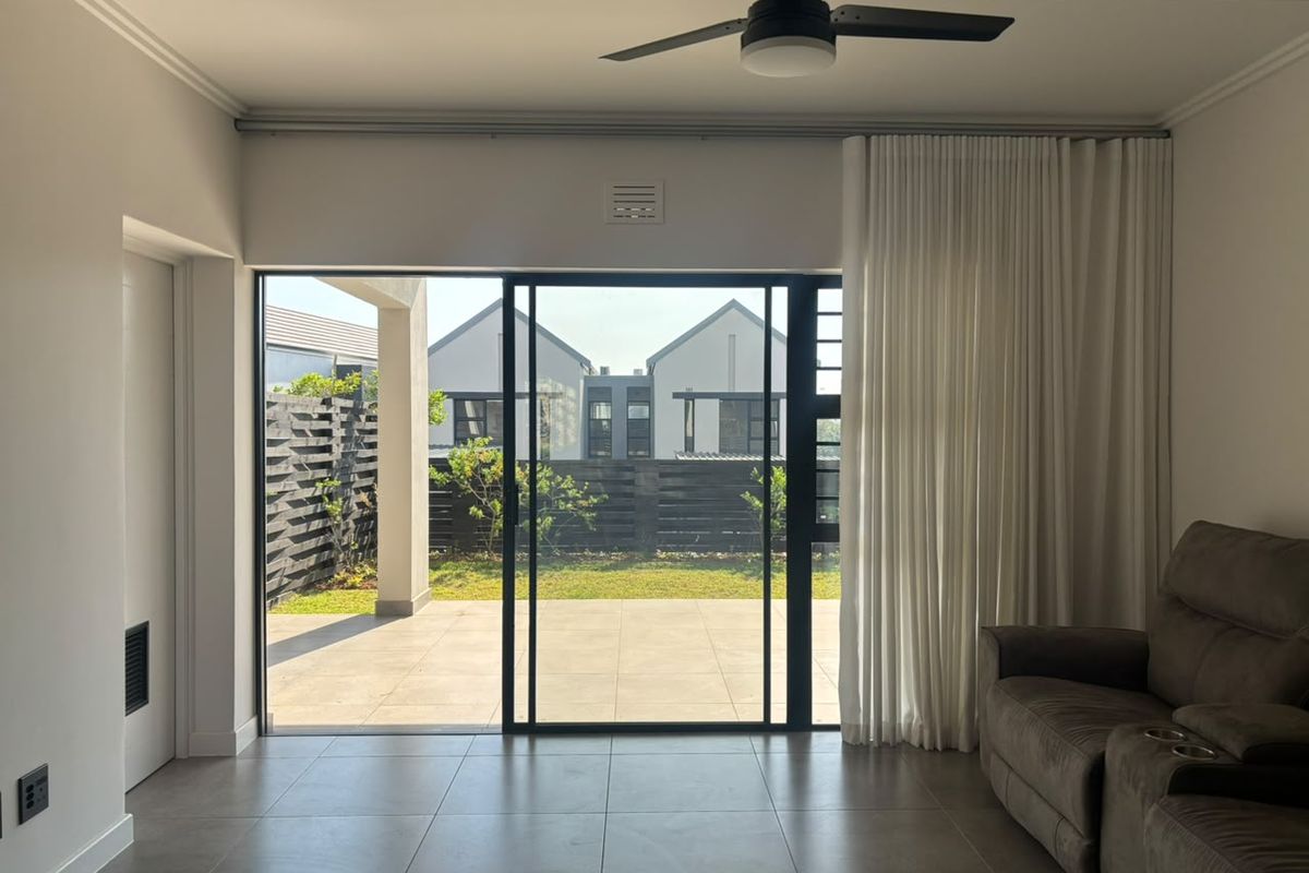 A bright living room featuring large sliding glass doors that open onto a paved patio and garden area, complemented by modern tiled flooring.