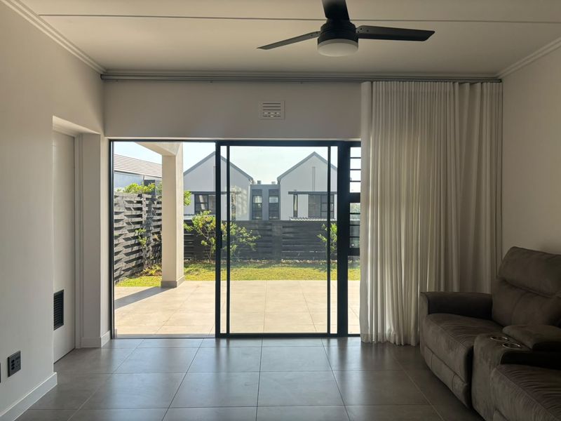 A bright living room featuring large sliding glass doors that open onto a paved patio and garden area, complemented by modern tiled flooring.