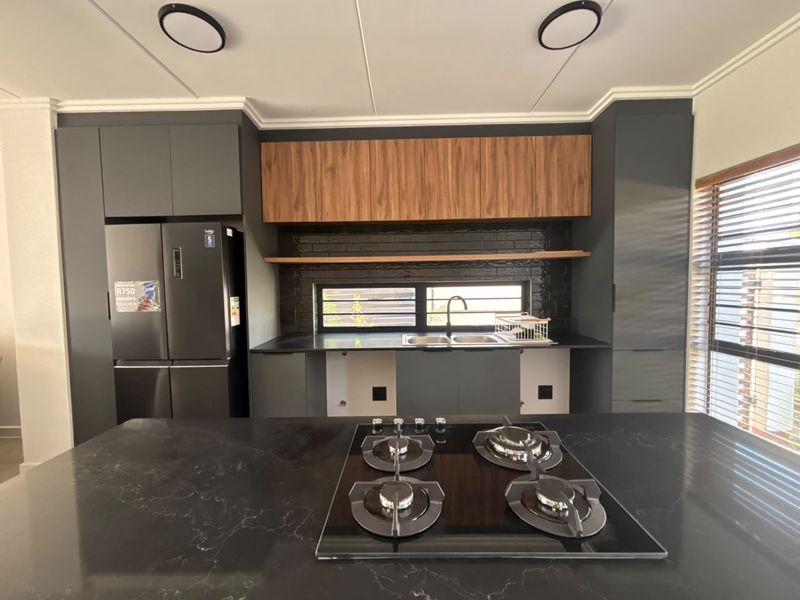 Modern kitchen featuring dark cabinetry, stone countertops, a central gas cooktop, and a stylish subway tile backsplash with integrated shelving.