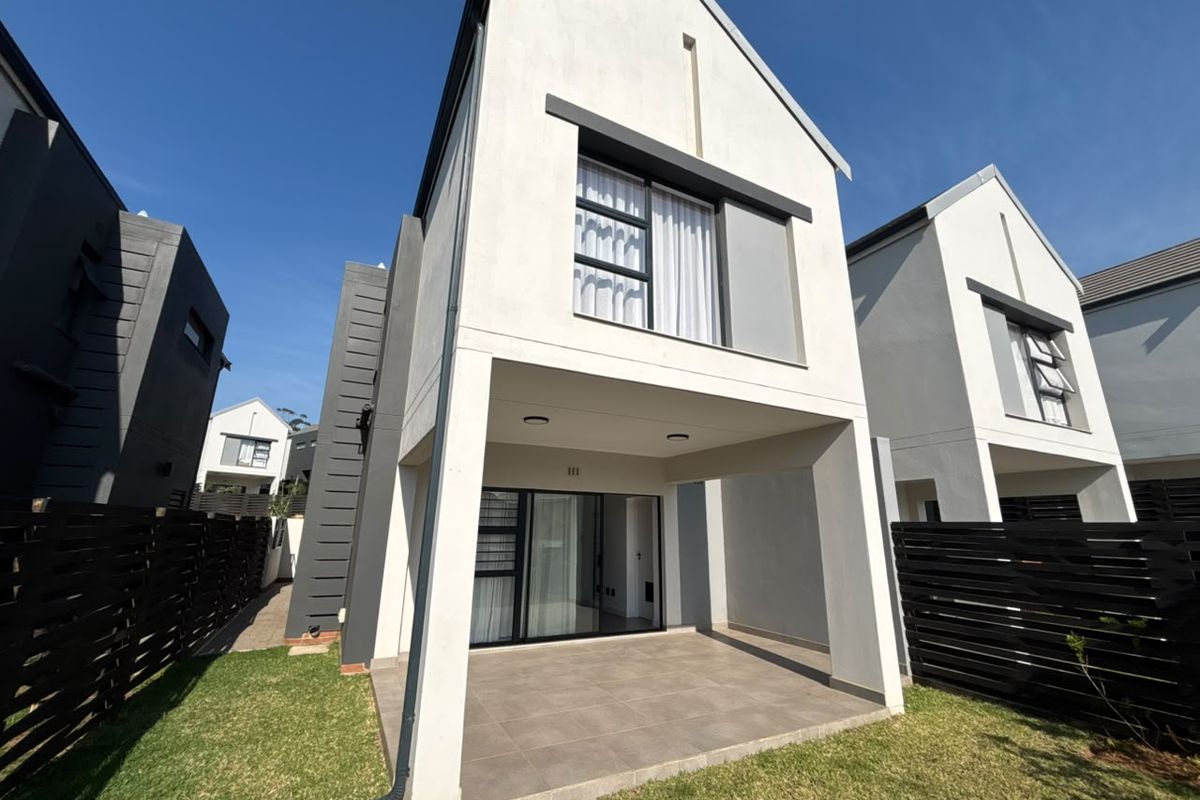 Rear view of a modern townhouse featuring a covered tiled patio, sliding glass doors, and a private garden area with timber fencing.