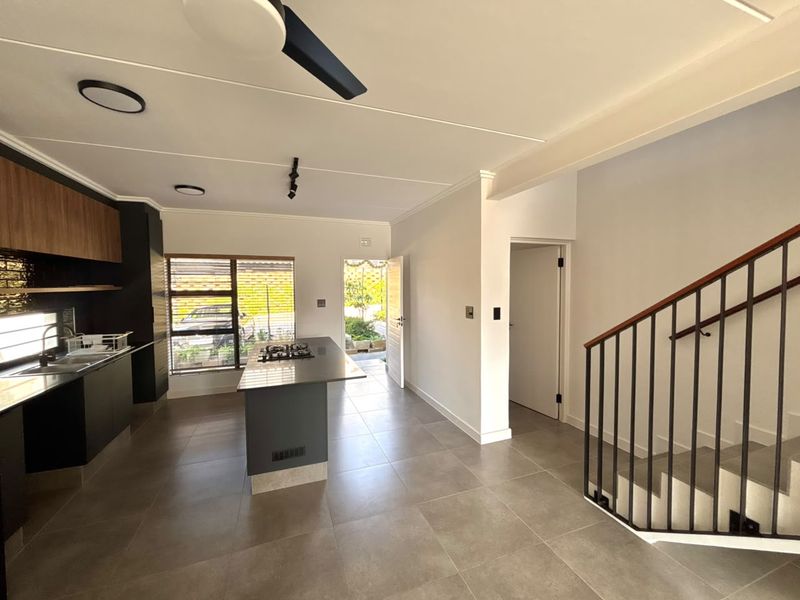 Modern open-plan kitchen and living area featuring sleek cabinetry, a central island with a gas hob, tiled floors, and a staircase with metal railings.
