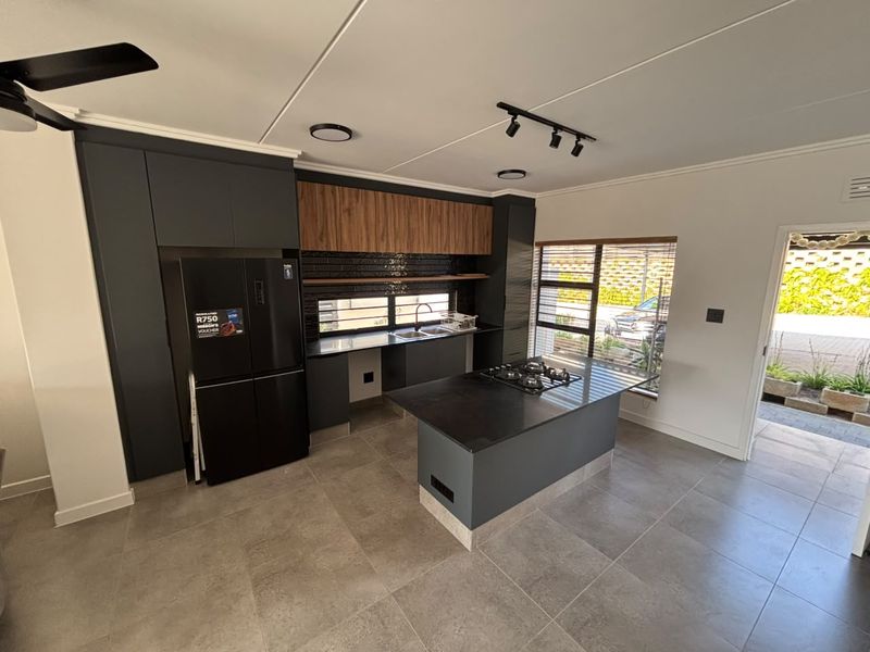 Modern kitchen featuring dark cabinetry, a central island with a gas hob, tiled flooring, and direct access to the exterior.