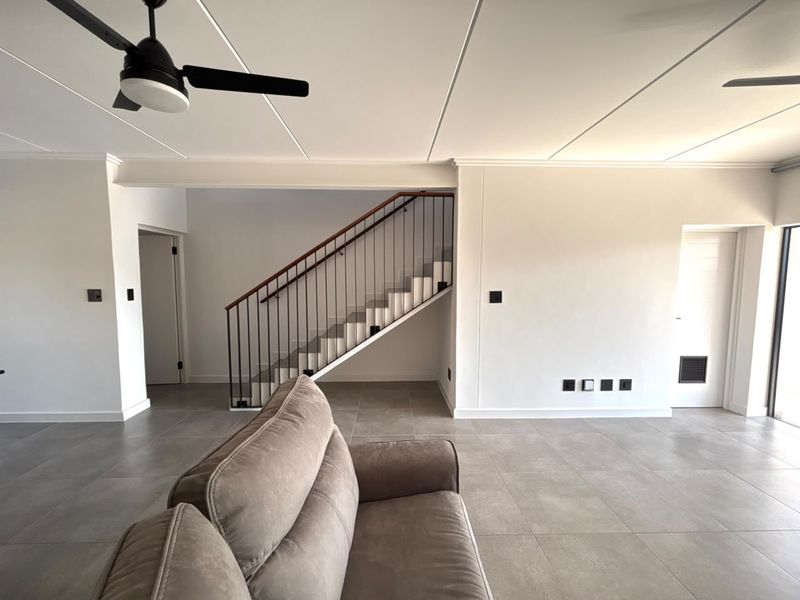Spacious living area featuring modern tiled flooring, a central staircase with a metal balustrade, and a ceiling fan, offering a clean, contemporary aesthetic.