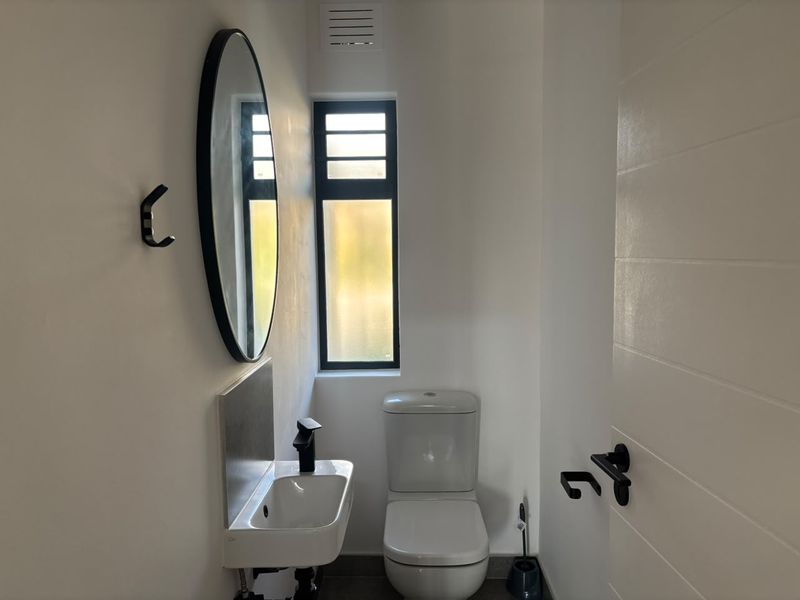 A modern, minimalist guest bathroom featuring a wall-mounted basin, black fixtures, and a clean, contemporary aesthetic.