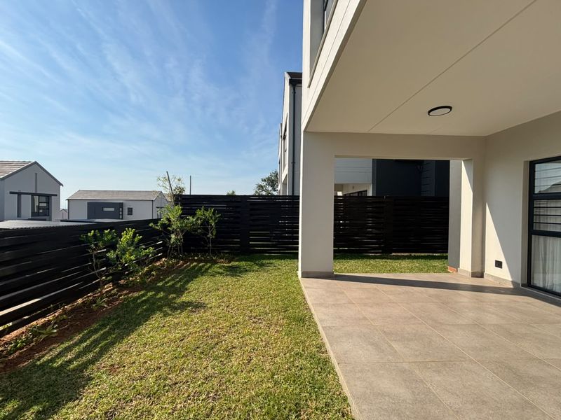 A modern covered patio area featuring tiled flooring and recessed lighting, overlooking a private garden with timber slat fencing.