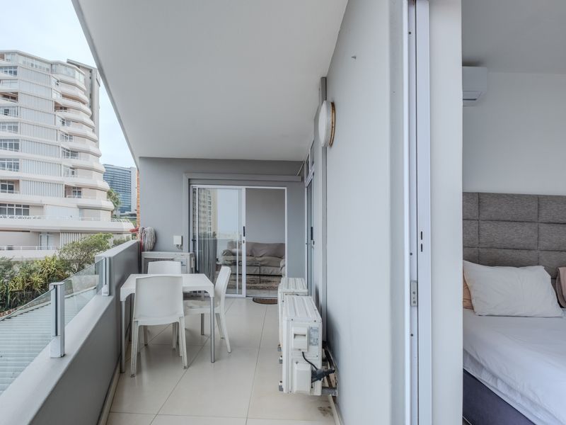 A covered balcony featuring tiled flooring, a glass balustrade, and direct access to the interior living space and bedroom through sliding glass doors.
