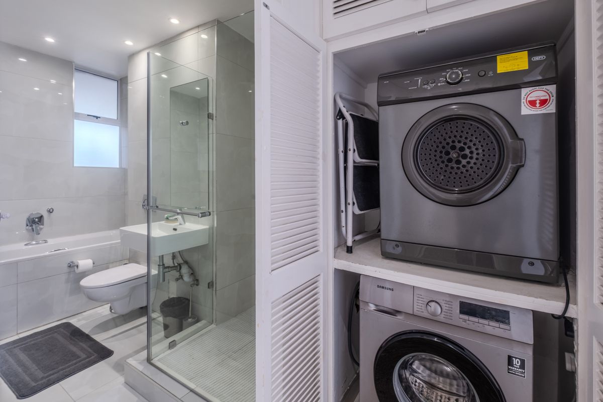 Modern bathroom featuring a glass-enclosed shower, wall-mounted basin, bathtub, and a convenient integrated laundry cupboard with stacked appliances.