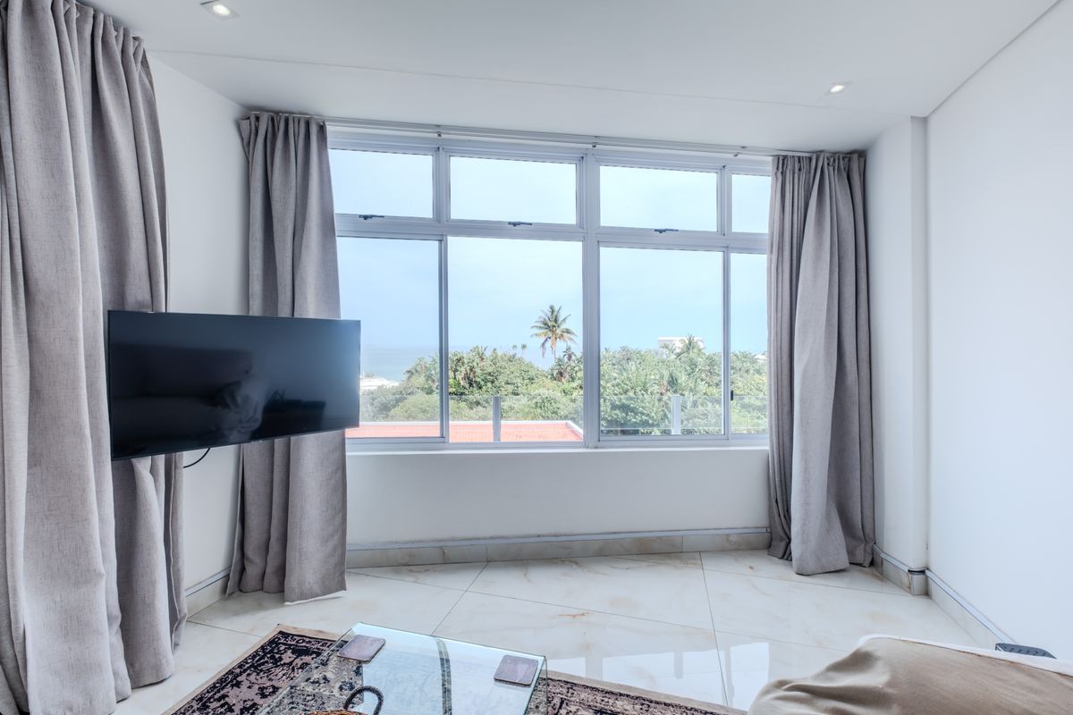 Bright living room featuring large format floor tiles, recessed downlights, and expansive windows offering a pleasant outdoor view.