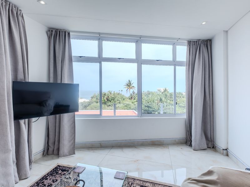 Bright living room featuring large format floor tiles, recessed downlights, and expansive windows offering a pleasant outdoor view.