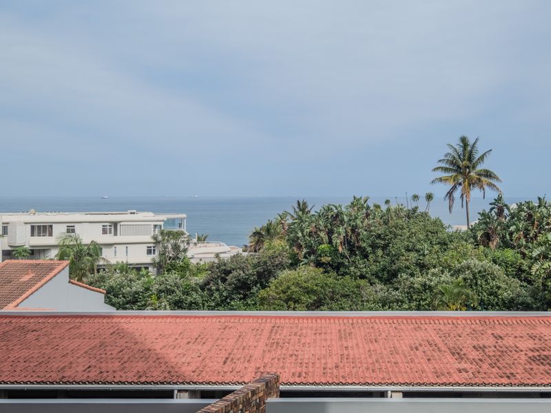 A scenic elevated view overlooking lush coastal vegetation and the ocean, featuring a prominent tiled roof in the foreground.