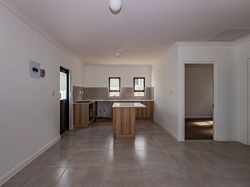 Open-plan kitchen area featuring modern wood-finish cabinetry, a central island, tiled flooring, and neutral finishes, providing a clean and functional space.