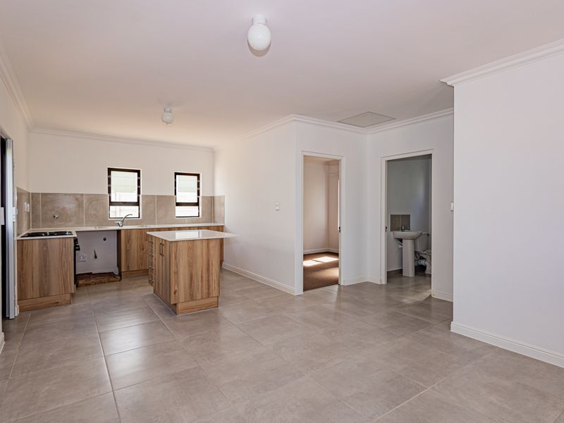 Open-plan kitchen and living area featuring modern wood-look cabinetry, stone countertops, tiled flooring, and an adjacent bathroom with a pedestal basin.