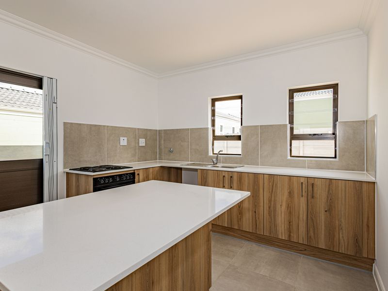 Modern kitchen featuring wood-finish cabinetry, stone countertops, a gas hob, and a tiled splashback, with direct access to the exterior.