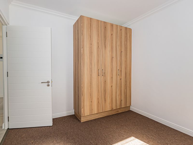 A clean, neutral bedroom featuring fitted wood-grain built-in wardrobes, carpeted flooring, and crisp white walls with decorative cornice detailing.