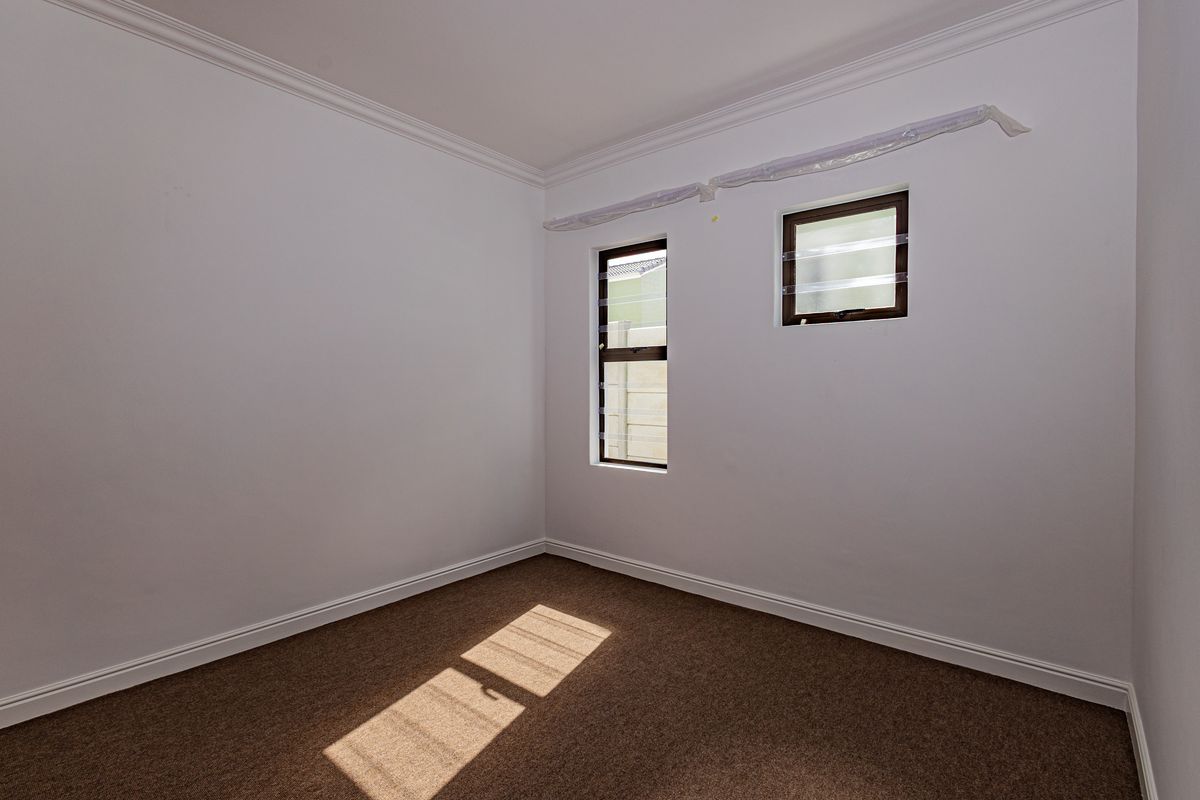 A clean, empty bedroom featuring neutral carpet flooring, crown molding, and louver windows, providing a blank canvas for personalization.