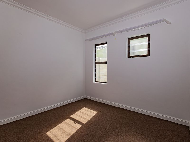 A clean, empty bedroom featuring neutral carpet flooring, crown molding, and louver windows, providing a blank canvas for personalization.