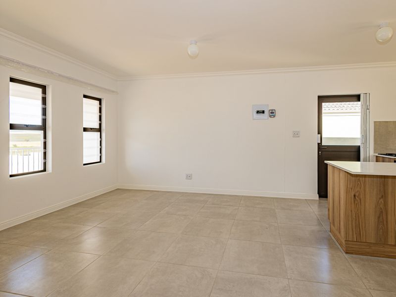 An open-plan living area featuring neutral tiled flooring, louver windows, and a modern kitchen island, providing a clean and versatile space.