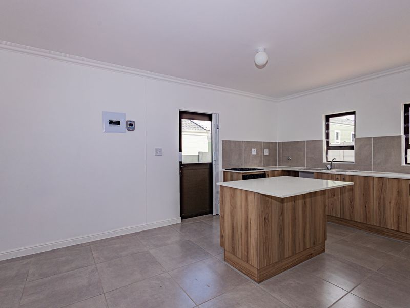 A modern, empty kitchen featuring wood-finish cabinetry, stone countertops, a central island, and tiled flooring with direct access to the exterior.