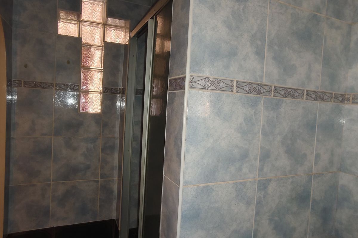 A bathroom featuring dated blue ceramic wall tiles, a shower enclosure, and a decorative glass block window detail.