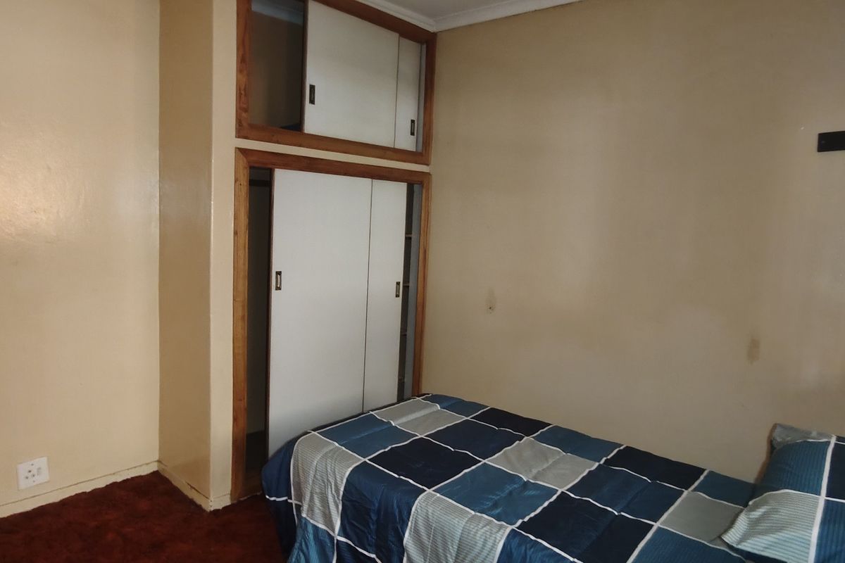 A bedroom featuring built-in wardrobes with overhead storage and carpeted flooring, requiring cosmetic updates to the wall finishes.